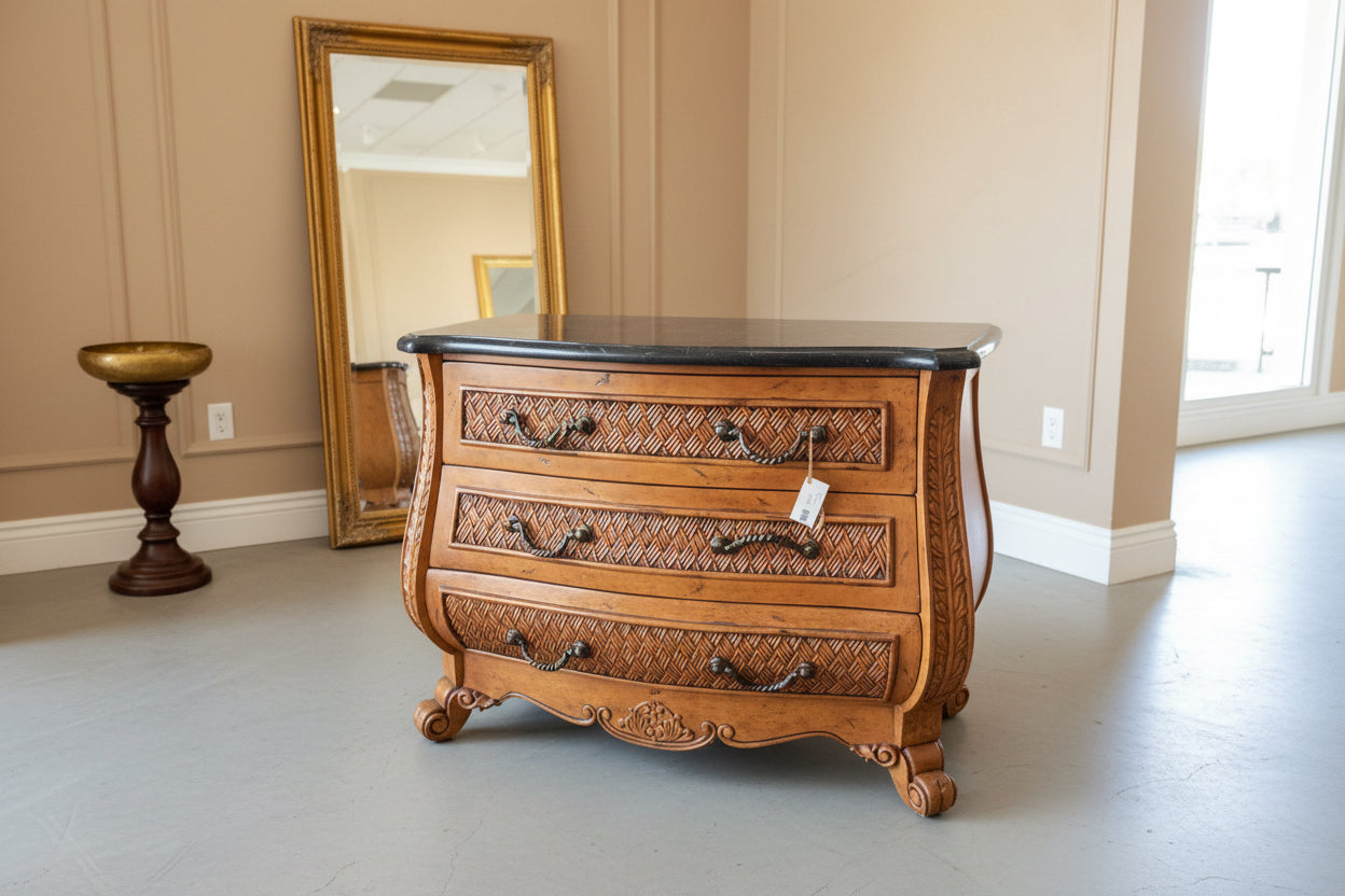 Wooden chest of drawers with decorative carvings on a concrete floor.